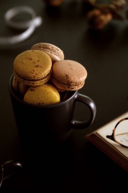 Sade kahve fincanındaki çikolatalı badem kurabiyelerinin yanında çalışma odasında bir kitap ve gözlük.