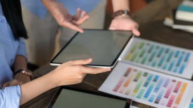 Projelerinde danışmanlık yapan genç tasarımcı takımının görünümünü kapat. Tablet ve renk örneklerini ahşap masa üzerinde hazırla.  