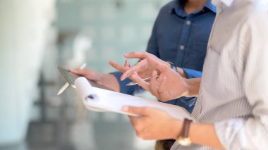 İki iş adamının cam duvar toplantı odasında dikilirken tablet ve belge dosyasıyla yaptıkları çalışmalara danışmanlık yapmalarının yan görüntüsü