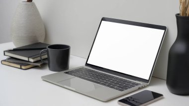 Boş ekran dizüstü bilgisayar, akıllı telefon, ofis malzemeleri ve beyaz masa süslemeleri ile asgari çalışma alanı görüntüsü 