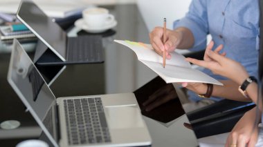 İki iş adamının görevlerini not defteri, dizüstü bilgisayar ve dijital tabletle kara masanın üzerinde tartışırken yan görünümü