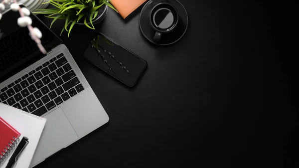 Top view of trendy workspace with laptop , smartphone, office supplies and copy space on black desk