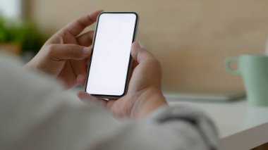 Basit bir çalışma alanında otururken boş ekran akıllı telefonu kullanan serbest çalışan bir erkeğin görüntüsü.