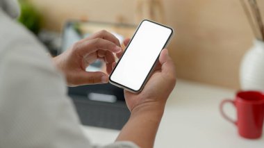 Basit bir çalışma alanında çalışırken erkek tasarımcının boş ekran akıllı telefonuna dokunuşunun kırpılmış görüntüsü