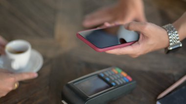 Erkek müşterinin akıllı telefonu kullanarak kafeteryadaki ahşap masa üzerindeki ödemeyi kestiği görüntüler. 