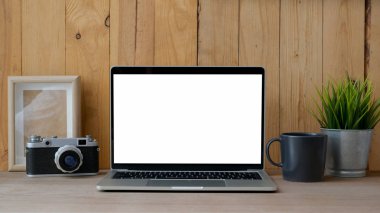 Modern kırsal duvarlı ahşap masa üzerindeki boş ekran dizüstü bilgisayar, kamera ve dekorasyonla antika çalışma alanının görüntüsünü kapat