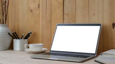 Boş ekran laptop, ofis malzemeleri ve ahşap masa üzerindeki ahşap duvar arka planlı dekorasyonla çağdaş çalışma alanının kırpılmış görüntüsü. 