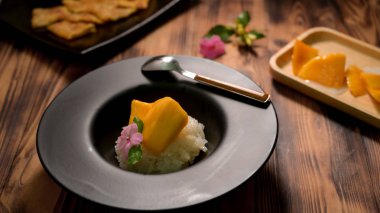 Siyah tabakta pirinç ve ahşap masada Roti ile kesilmiş Tayland mangosu.