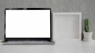 Model, dizüstü bilgisayar, çerçeve ve kaktüs tenceresi ile beyaz masa ve gri çatı katı duvarı olan minimal işyeri manzarasını kapat 