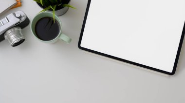 Boş tablet, kamera, kahve fincanı ve beyaz masadaki boşluğu kopyalayan fotoğrafçı çalışma alanının üst görüntüsü  