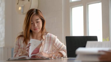 Genç üniversiteli kızın basit oturma odasında final sınavı için kitap okumasına yakından bakın.