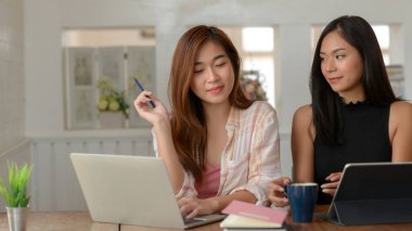 Kütüphanede dizüstü bilgisayar, tablet ve kırtasiye ile projelerini hazırlayan iki üniversiteli kızın yakın görüntüsü 