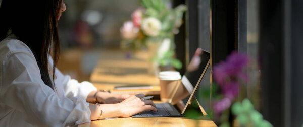 Cropped shot of young woman university student focusing on her assignment with digital tablet on wooden counter bar in coffee shop
