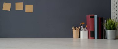 Kitaplar, sanatçı gereçleri, dekorasyonlar ve gri duvarlı beyaz masa üzerindeki kopya alanı ile modaya uygun çalışma alanı. 
