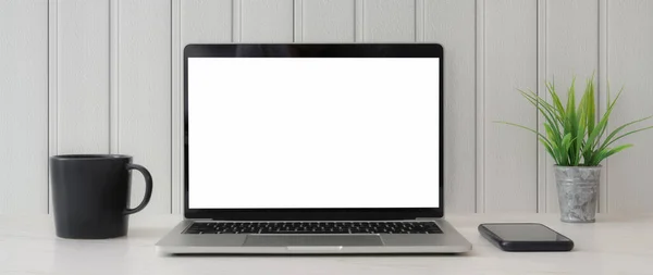 Boş ekran dizüstü bilgisayar, akıllı telefon, kahve fincanı ve beyaz tahta arka planlı ağaç tepsisiyle en az çalışma alanı görüntüsü.  