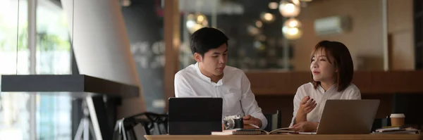 Cropped shot of two businesspeople discussing on their work with computer laptop on white desk in modern office room