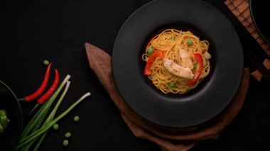 Top view of Schezwan Noodles or Chow Mein with vegetable and chicken in black plate on black table  clipart