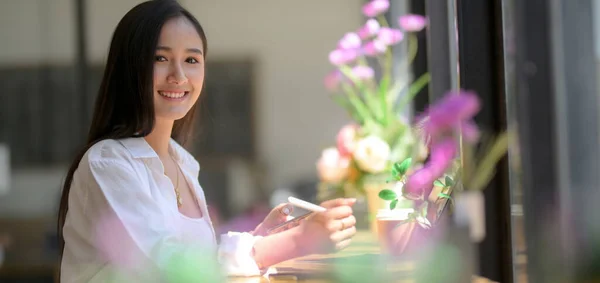 Side view of smiling female university student sitting at wooden counter bar and working with digital tablet