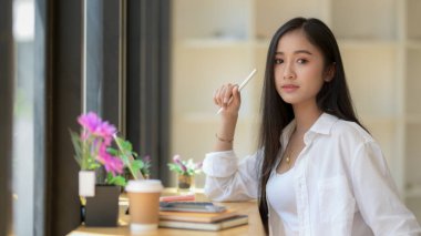 Dijital tablet ve kırtasiye malzemeleriyle uğraşırken, üniversitedeki kız öğrencinin ahşap tezgahta oturmasını yakından izle.