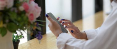 Kafedeki ahşap tezgahta kahve beklerken akıllı telefon kullanan genç bir üniversite öğrencisinin görüntüsü.