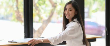 Gülümseyen genç bir üniversite öğrencisinin kahve dükkanındaki tezgahta oturup rahatlarken çekilmiş görüntüsü.