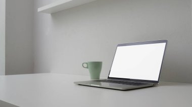 Boş ekran dizüstü bilgisayar, kupa ve kopya alanı beyaz masadaki beyaz duvarlı minimal çalışma alanı görüntüsü 