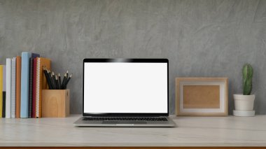 Boş ekran laptop, dekorasyonlar, kitaplar ve kırtasiye malzemeleriyle modern çalışma alanının görünümünü gri çatı katı duvarlı mermer masa üzerinde kapat 