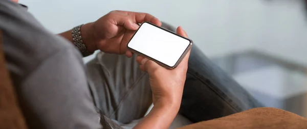 拍下了一个男人坐在现代客厅里拿着水平空白屏幕智能手机的照片 — 图库照片