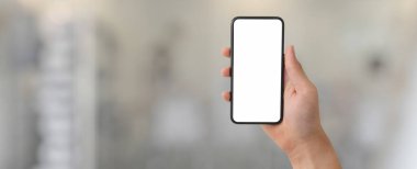 Bulanık cam bölme ofis arka planında boş ekran akıllı telefon gösteren bir adamın kırpılmış görüntüsü.