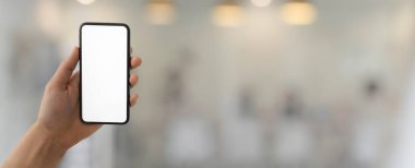 Bulanık cam duvarlı ofis arka planında elinde boş ekran akıllı telefon olan bir adamın kırpılmış görüntüsü.