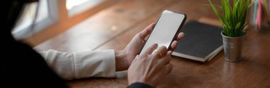 Boş ekran akıllı telefonuna dokunan serbest çalışan bir kadının basit bir çalışma alanında otururken çekilmiş görüntüsü. 