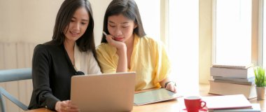 İki üniversiteli kızın yaklaşan sınavlarını rahat çalışma alanında dizüstü bilgisayar ve tabletle hazırlamak için birlikte okuduğu görüntüyü kapat.