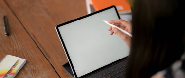 Kütüphanedeki ahşap masada boş ekran laptopuyla ödev yapan genç kız öğrencinin kırpılmış görüntüleri. 