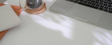 Laptop, ofis malzemeleri, kahve fincanı ve beyaz masadaki fotokopi alanı.  