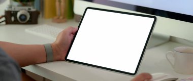 Beyaz masada elinde boş ekran tableti olan bilgisayar aygıtı ve kahve fincanı olan bir adamın kırpılmış görüntüsü.