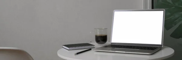 Close up view of portable workspace with blank screen laptop, supplies and coffee cup on white circle table