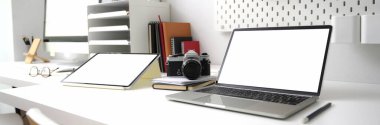 Boş ekran dijital cihazlarla, ofis malzemeleriyle ve beyaz masadaki kamerayla çekilmiş bir fotoğraf. 