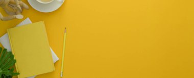 Günlük defterleri, çay fincanı, dekorasyon ve sarı masa arkaplanındaki kopyalama alanı ile yaratıcı çalışma alanının en üst görünümü 