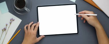 Gri masa arkaplanındaki tablet ve diğer malzemelerle evden çalışan kadın serbest çalışanın genel görüntüsü.