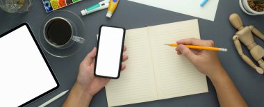 Model akıllı telefon, tablet, eskiz kâğıdı ve gri masa arkaplanındaki tasarımcı malzemeleri üzerinde çalışan kadın tasarımcının genel görüntüsü.