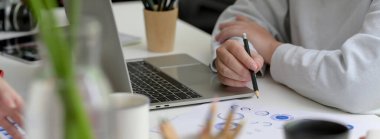 Dizüstü bilgisayarla çalışan ve ofis malzemeleriyle beyaz masadaki iş haritasını okuyan bir iş kadını görüntüsü.