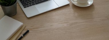 Laptop, kırtasiye malzemesi, kahve fincanı ve ahşap masadaki fotokopi alanı.   