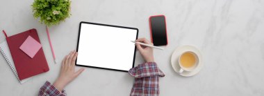 Boş ekran tableti, akıllı telefon, malzeme ve mermer masada çay fincanı üzerinde çalışan kadın serbest çalışanın üst görüntüsü.  