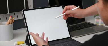 İki tasarımcının, projelerini rahat çalışma ortamında tartışırken çekilmiş görüntüleri beyaz masadaki tablet, dizüstü bilgisayar ve tasarımcı malzemeleriyle