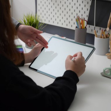Modayı takip eden iş yerinde meslektaşıyla beyin fırtınası yaparken kadın tasarımcının maket tablet üzerinde çalışırken çekilmiş bir fotoğrafı.