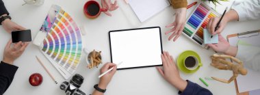 Tasarımcı takımı, beyaz masadaki tablet, akıllı telefon ve tasarımcı malzemeleriyle projelerine minimum çalışma alanında danışmanlık yapıyor 