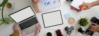 Ekip oluşturup evrak işlerini birlikte analiz ederken beyaz masada dijital cihazlar ve ofis malzemeleriyle çekilen bir çekim. 