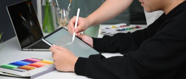 Beyaz masa üzerinde tablet, dizüstü bilgisayar ve tasarımcı malzemeleriyle rahat çalışma alanında birlikte çalışan iki kadın tasarımcının yan görüntüsü
