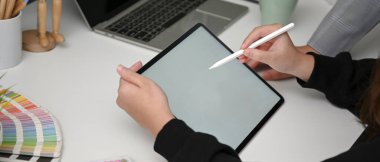 Tasarımcının rahat çalışma alanında beyaz masa üzerinde tasarım malzemesi, tablet, dizüstü bilgisayar ve tasarım malzemeleriyle çalışırken çekilmiş görüntüsü.