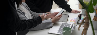 Modern çalışma ortamında tasarım ekibinin projelerine tablet, dizüstü bilgisayar ve akıllı telefonla danışmanlık yapmasının yan görüntüsü 